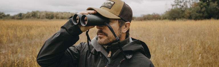 Birding With Bushnell Man in grassy field looking through Bushnell Binoculars