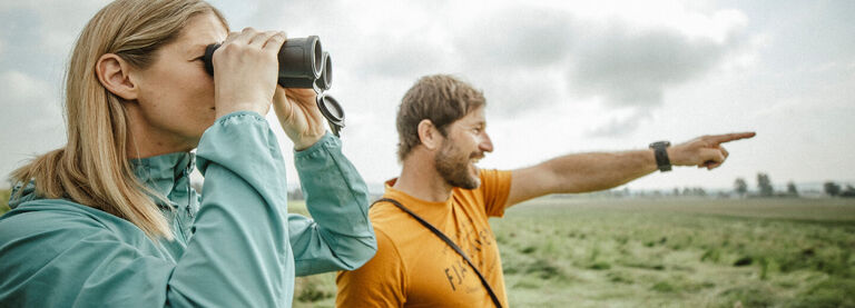Bushnell Birding Binoculars and Accessories Couple in an open grassy birding with a pair of binoculars