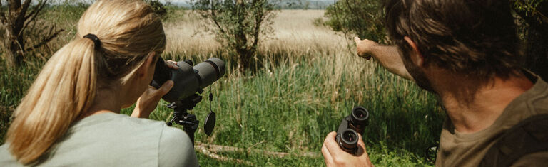 Birding With Bushnell Man and woman in grassy filed using Bushnell Spotting Scope and Binoculars